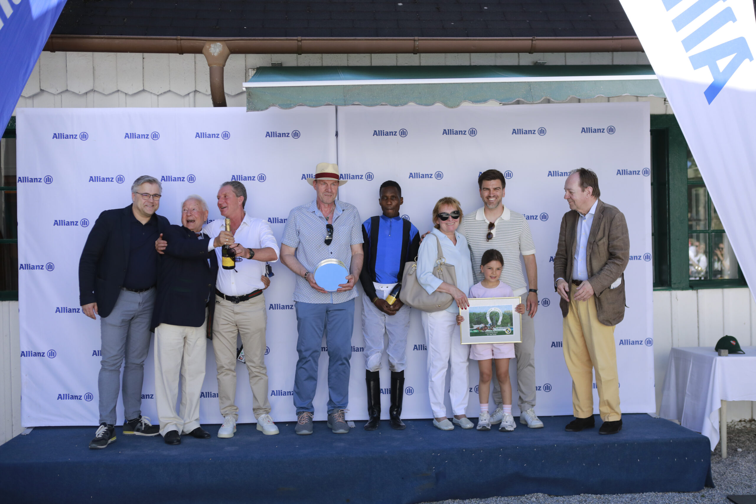 23.05.2026 - Munich; Winners presentation with Sascha Multerer (General Secretary Muenchener Rennverein e.V.), Hermann Koll, John David Hillis, Eduardo Pedroza, Dagmar Kuplent, representative of the sponsor and Freiherr Dr. Georg von Gumppenberg (Chairman Muenchener Rennverein e.V.) after winning the Preis vom Allianz Familienfest with Launching Percy at Munich-Racecourse/Germany. Credit: Lajos-Eric Balogh/turfstock.com